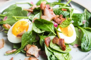 A spinach salad with hot bacon dressing, bacon, and eggs.