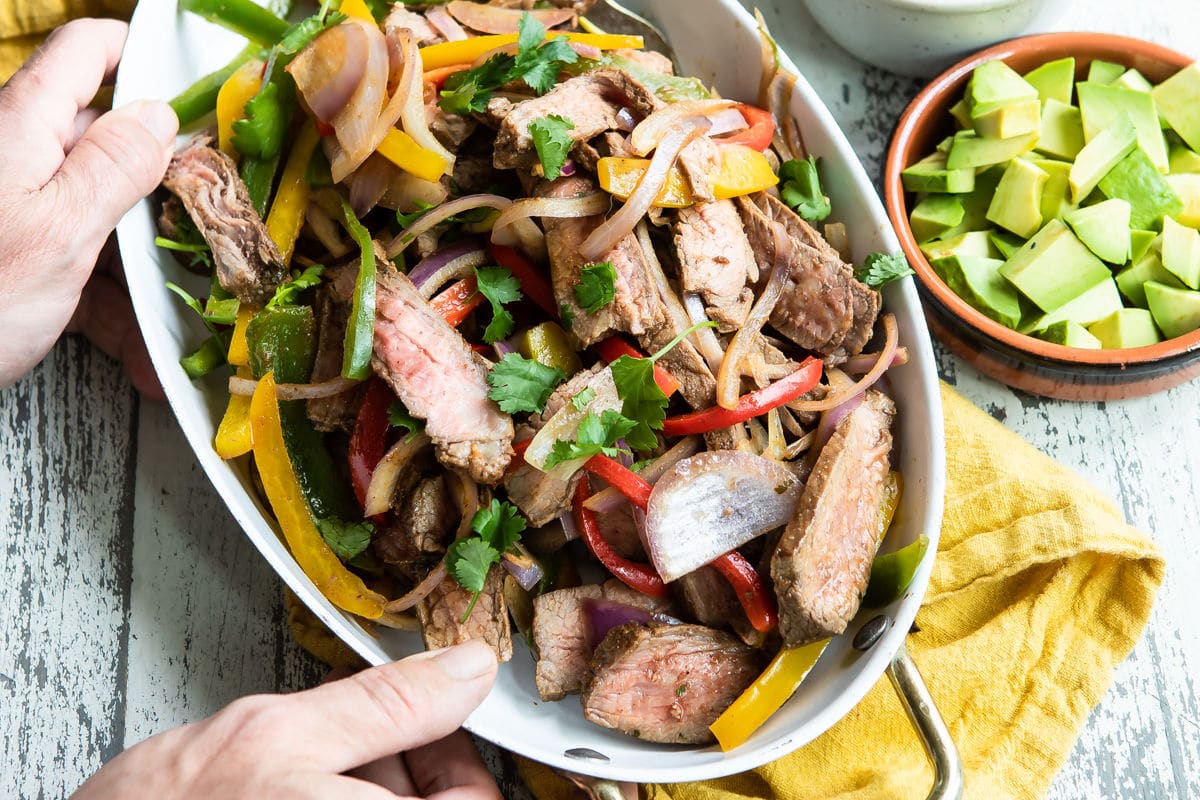 Steak fajitas in a white serving dish.