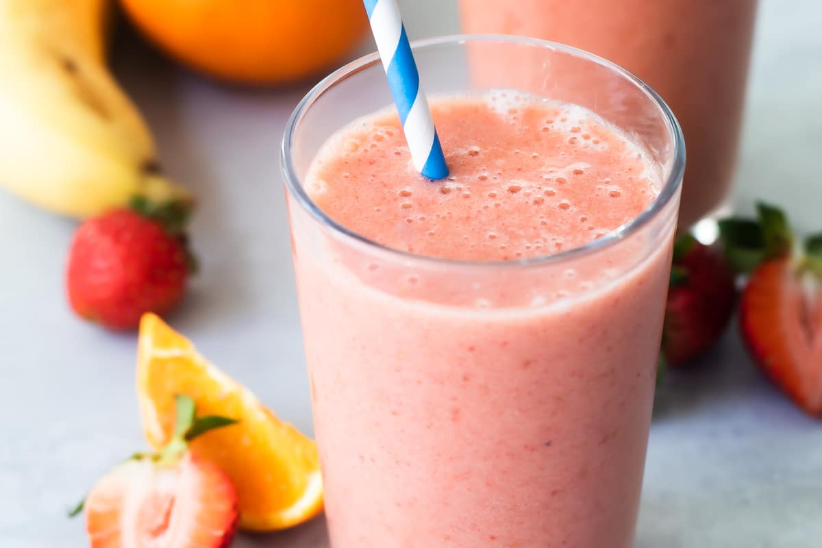 2 glasses with straws of Strawberry Citrus Ginger Smoothie next to fresh fruit.