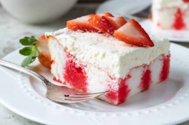 A slice of strawberry jello poke cake on a white plate.