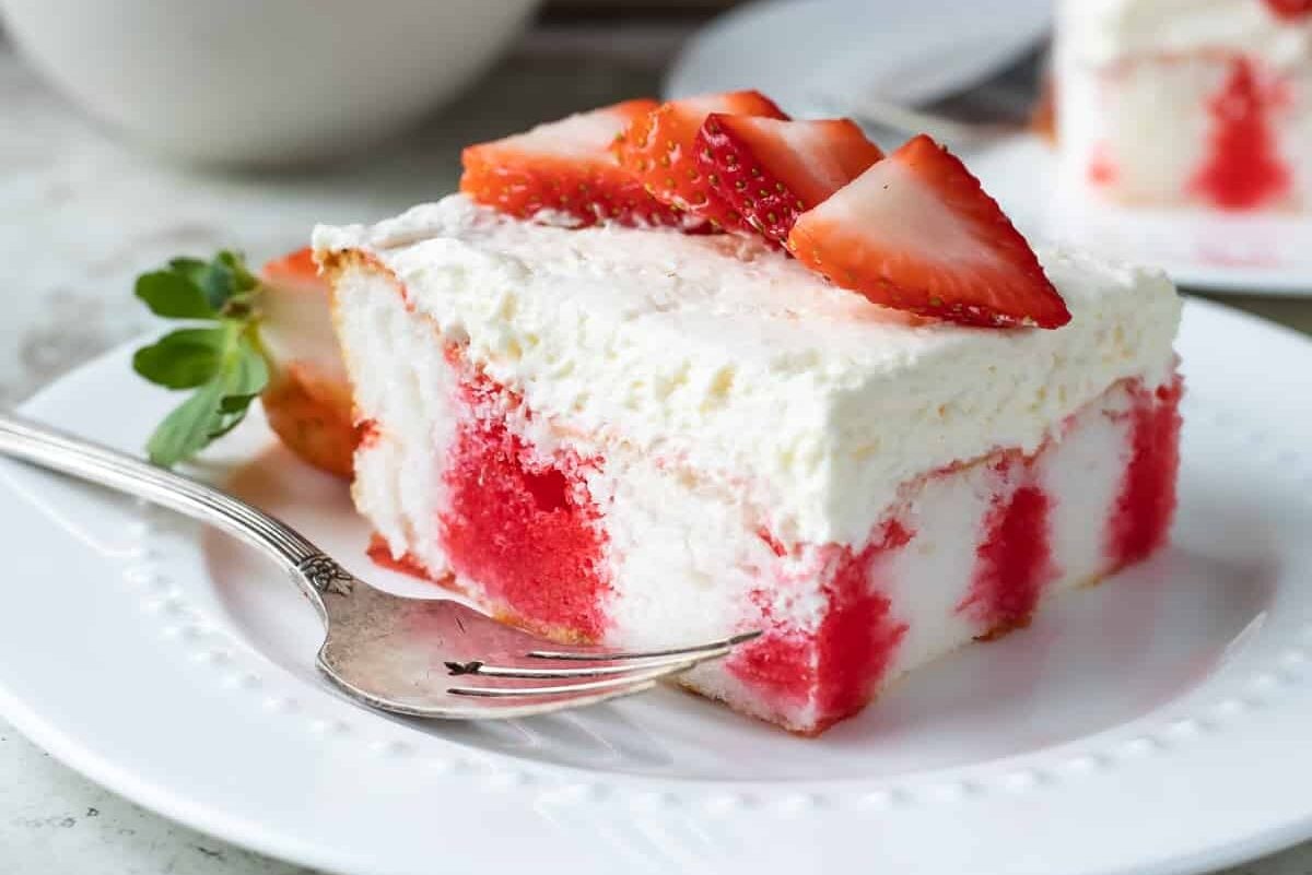 A slice of strawberry jello poke cake on a white plate.