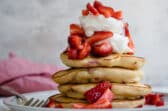 A stack of strawberry pancakes topped with whipped cream strawberries.