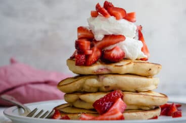 A stack of strawberry pancakes topped with whipped cream strawberries.