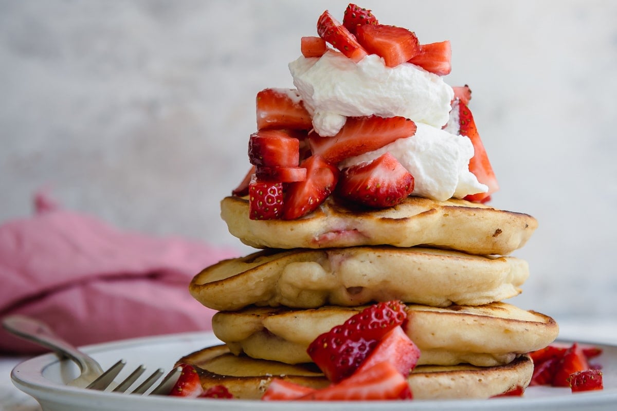 A stack of strawberry pancakes topped with whipped cream strawberries.
