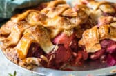 A strawberry rhubarb pie in a pie pan with one slice removed.