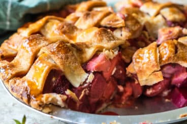 A strawberry rhubarb pie in a pie pan with one slice removed.