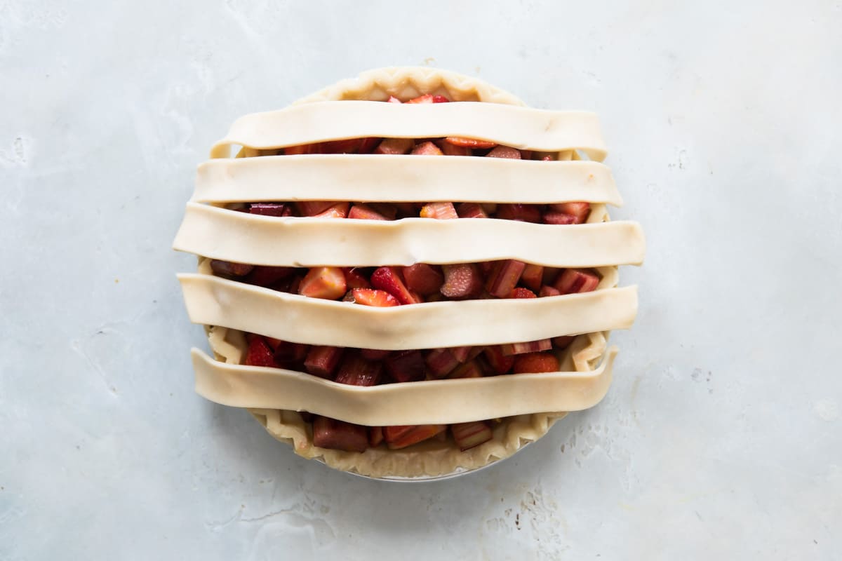 A strawberry rhubarb pie before being baked with lattice incomplete.