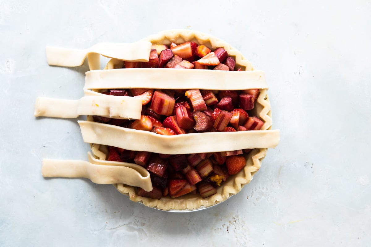 A strawberry rhubarb pie before being baked with lattice incomplete.