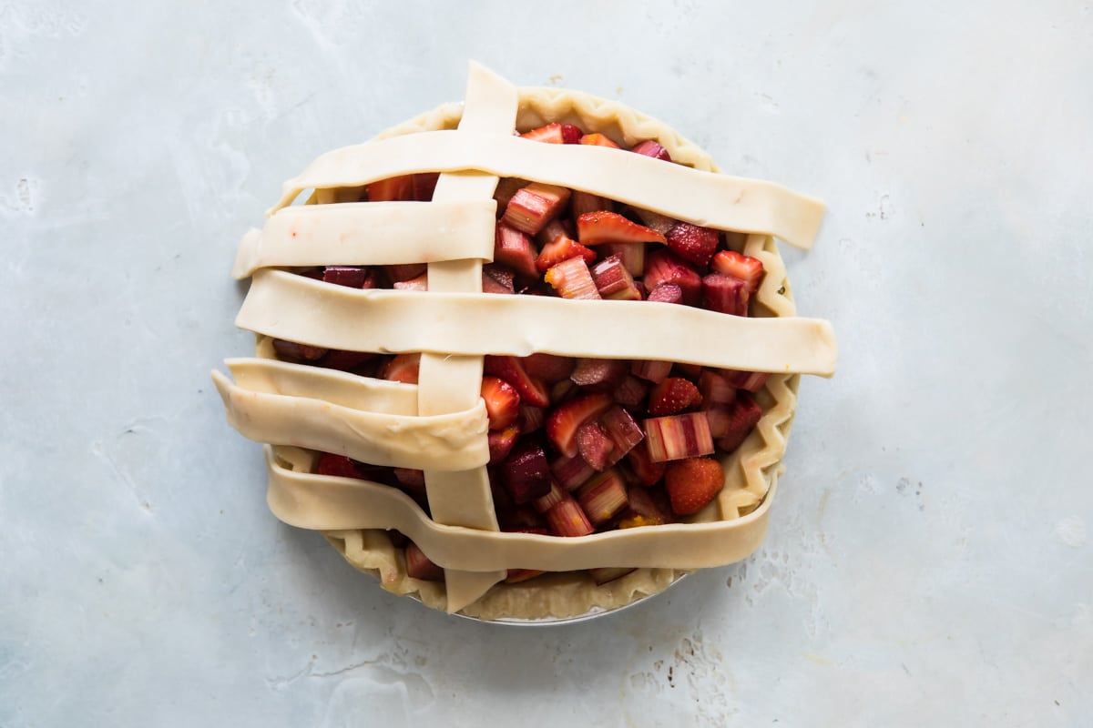 A strawberry rhubarb pie before being baked with lattice incomplete.