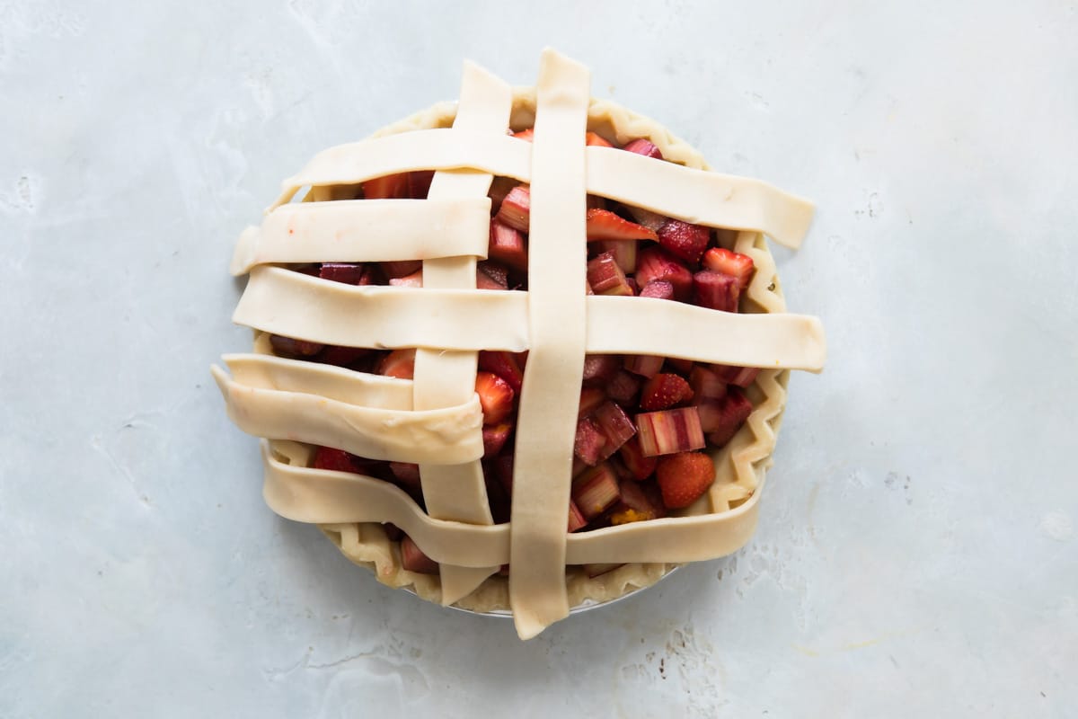 A strawberry rhubarb pie before being baked with lattice incomplete.