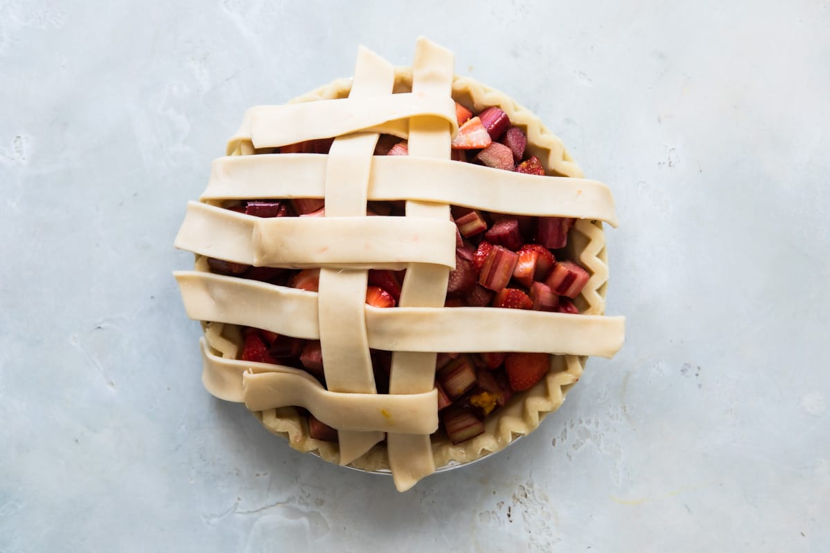 A strawberry rhubarb pie before being baked with lattice incomplete.