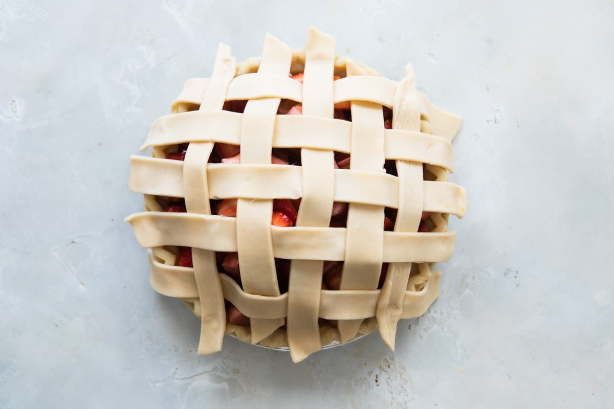 A strawberry rhubarb pie before being baked with lattice not tucked in.