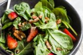 Strawberry spinach salad in a black bowl.