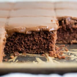 A pan of Texas sheet cake cut into squares and some squares removed from the pan.