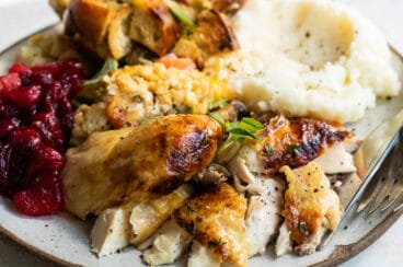 A plate of roasted Cornish hen, mashed potatoes, stuffing, vegetable casserole, and cranberry sauce.