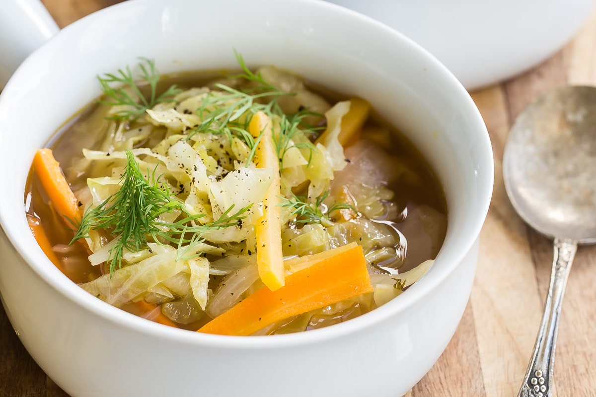 Cabbage Soup in two white bowls on a wooden cutting board.