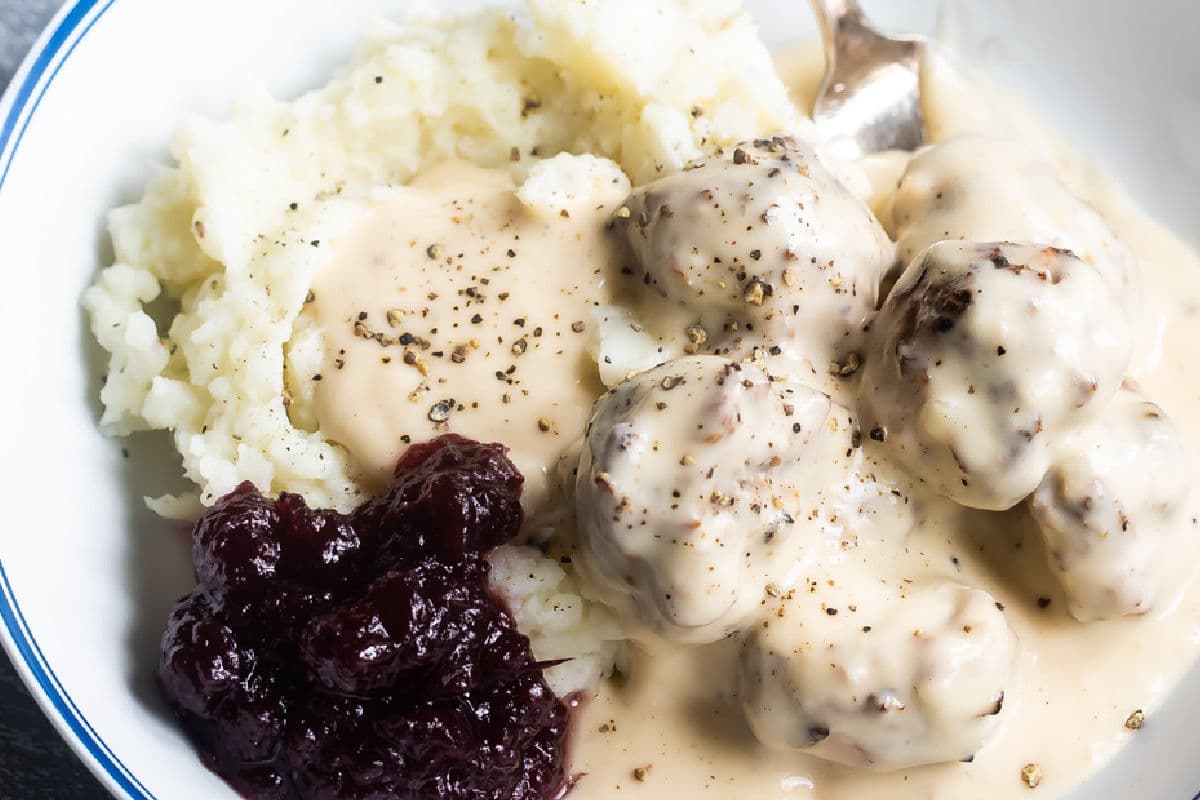 Swedish meatballs on plates with mashed potatoes, gravy, and cranberry sauce.