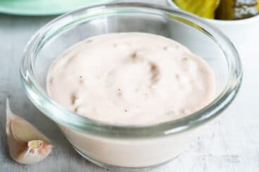Thousand Island dressing in a clear bowl on a countertop with pickles and lettuce in the background.