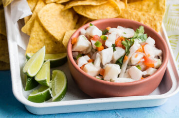 Taliapa ceviche in a pink bowl on a white platter with tortilla chips.
