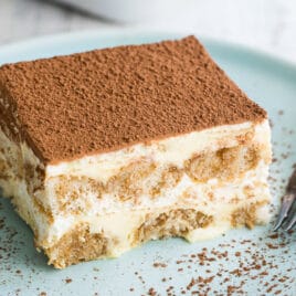 A piece of tiramisu on a blue plate with a fork.