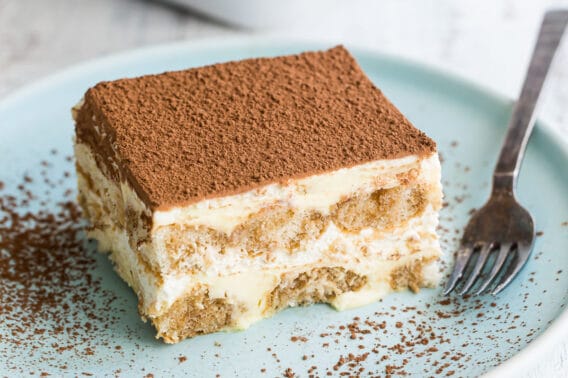 A piece of tiramisu on a blue plate with a fork.