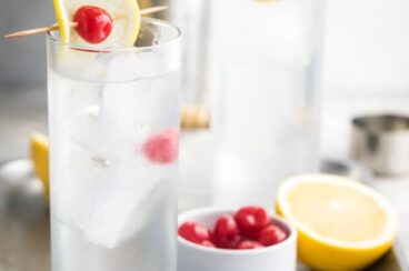 Tom collins in two clear glasses on a silver tray.