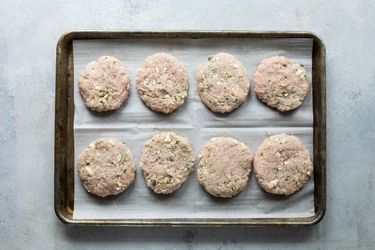 Turkey burgers on a parchment paper lined baking sheet before being cooked.