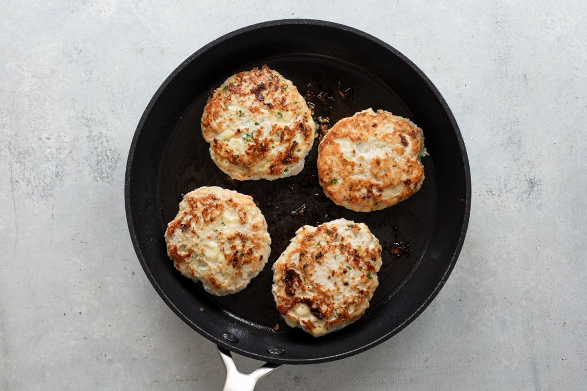 Turkey burgers being cooked in a black skillet.