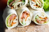 A pile of veggie wraps cut open on a cutting board.