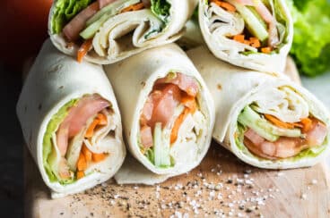 A pile of veggie wraps cut open on a cutting board.