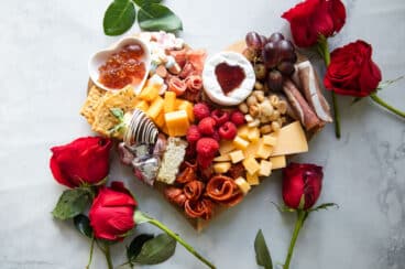 A fully-built Valentine's Day charcuterie board with roses around it.