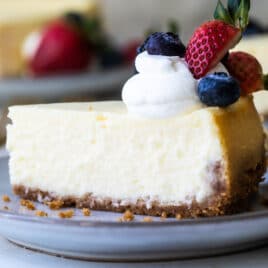 A plate of Vanilla Cheesecake with berries and whipped cream on top.