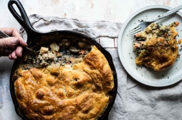 Vegetable pot pie in a cast iron skillet next to a plate with a serving of vegetable pot pie.