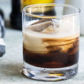 A white Russian cocktail with a bottle of Kahlua in the background.