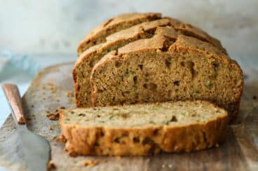 A loaf of zucchini bread partially cut into slices on a wooden cutting board.