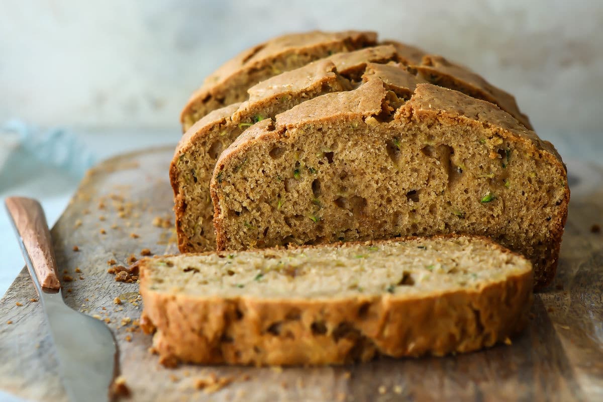 A loaf of zucchini bread partially cut into slices on a wooden cutting board.